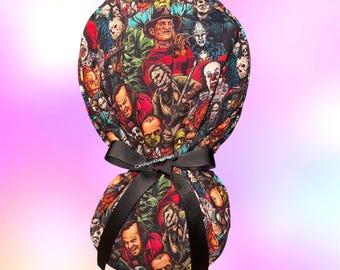 May include: A fabric scrub cap featuring a colorful all-over print of various horror movie characters, including Freddy Krueger and Pennywise. The cap has a gathered back secured with a black grosgrain ribbon tied in a bow at the center.