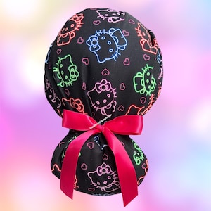 May include: A black scrub cap featuring a neon-style print of Hello Kitty characters in blue, green, and pink outlines, interspersed with small pink hearts. The cap is gathered at the back and secured with a bright pink satin ribbon bow.