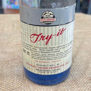 Puede incluir: Botella de limpiador "Try-it" de Stanley Home Products, vintage. La botella de vidrio tiene una tapa roja y una base azul. La etiqueta presenta el texto "Try-it" en escritura roja, junto con información del producto y el logotipo de Stanley Home Products.