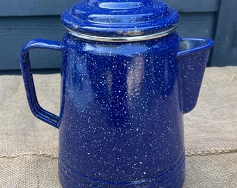 Cafetera vintage de metal esmaltado blanco con motas azules, estilo rústico o cabaña de camping.