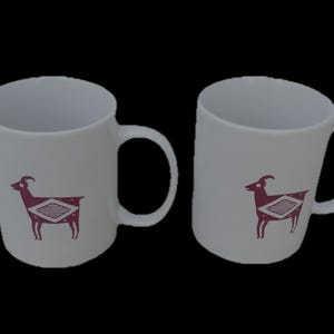 May include: Two white ceramic mugs with a maroon goat design. Each mug has a curved handle and a cylindrical shape. The goat design is a stylized illustration with geometric patterns.