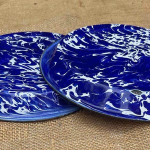 May include: Two blue and white enamelware plates with a marbled design. The plates have a dark blue rim and a white and blue pattern. The plates are round and appear to be vintage or antique.
