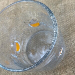 May include: A clear, cylindrical glass vase with a textured surface. The vase has small, irregular orange and gray accents. The rim of the vase is slightly uneven. The vase is empty.