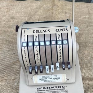 May include: Vintage beige Paymaster cash register with dollar and cent indicators. Features a crank handle and a series of numbered levers. The text on the register includes "Dollars", "Cents", and "Locked Protection".
