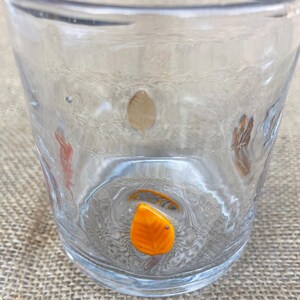 May include: A clear glass tumbler with a textured surface. The glass features decorative leaf-shaped accents in shades of orange and brown. The tumbler is designed for everyday use.