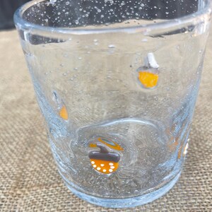 May include: A clear glass tumbler with a textured surface and small bubbles. The glass is decorated with orange, white, and brown acorn designs. The tumbler is suitable for serving beverages.