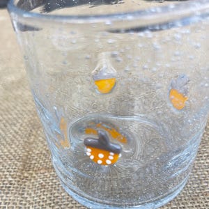 May include: A clear glass with a textured surface and small bubbles. The glass is decorated with orange and white acorn-shaped designs. The glass is likely used for drinking.