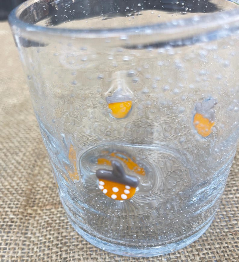 May include: A clear glass with a textured surface and small bubbles. The glass is decorated with orange and white acorn-shaped designs. The glass is likely used for drinking.