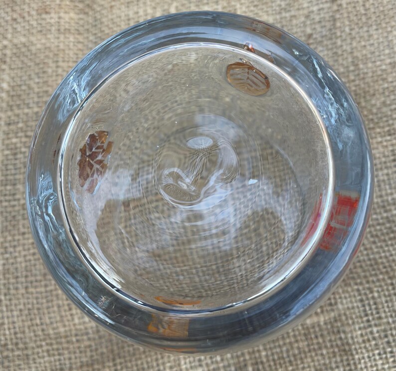 May include: A clear glass bowl with a wide rim, viewed from above. The bowl has a slight blue tint and features subtle leaf-like designs on the interior. The glass appears to be smooth and reflective, with a circular shape.