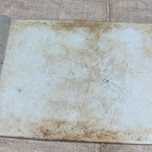 以下が含まれることがあります： 長方形のオフホワイトのベーキングシートで、縁が盛り上がっています。シートには茶色のシミや跡があり、使用感があります。縁は丸みを帯びており、わずかに盛り上がっており、グリップを提供します。シートはおそらくセラミックまたは同様の素材で作られています。