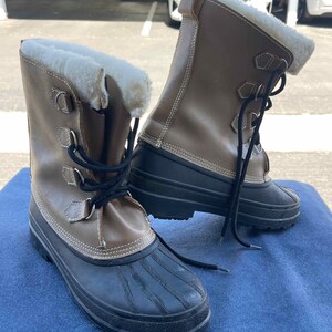 May include: A pair of brown leather winter boots with black rubber soles and white faux fur lining. The boots have laces and buckles.