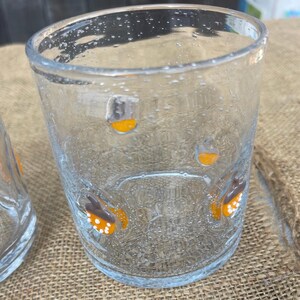 May include: Clear glass tumbler with a textured surface and small bubbles. The glass is decorated with orange and white butterfly designs. The tumbler is suitable for serving beverages.