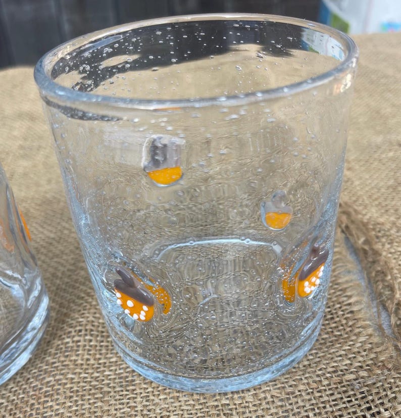 May include: Clear glass tumbler with a textured surface and small bubbles. The glass is decorated with orange and white butterfly designs. The tumbler is suitable for serving beverages.