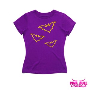 May include: Purple t-shirt with a design of three yellow bats.