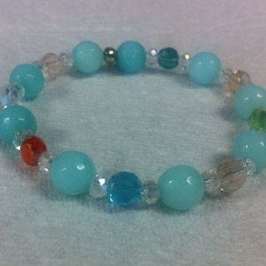 May include: A beaded bracelet featuring large, round, light blue beads interspersed with smaller, clear, and colorful beads. The bracelet has a mix of colors, including red, green, and blue, and is designed to be worn around the wrist.