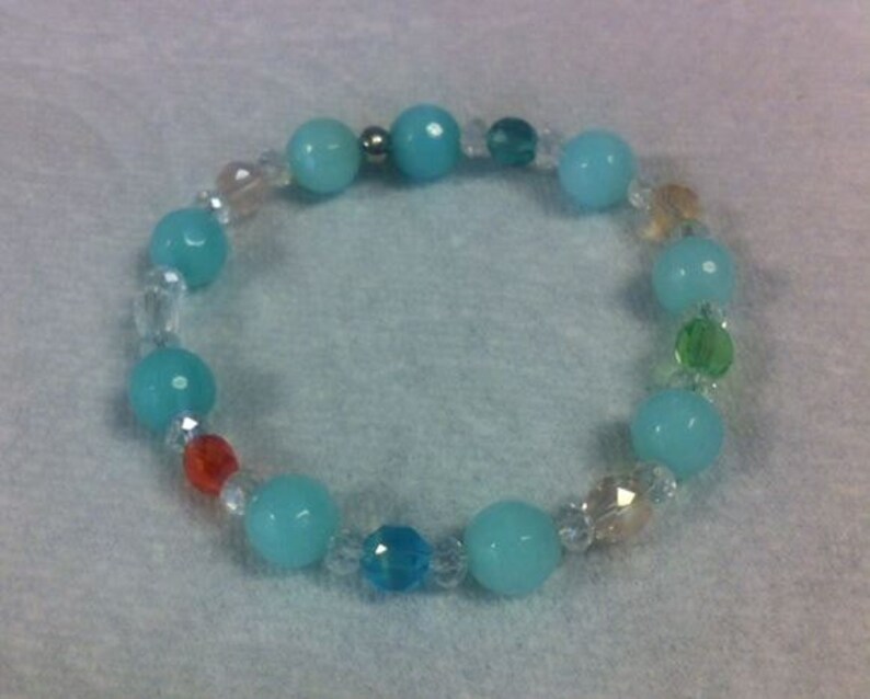 May include: A beaded bracelet featuring alternating turquoise and clear crystal beads, with accents of orange, green, and yellow beads. The bracelet is strung on a clear elastic cord and is suitable for everyday wear.