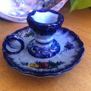 May include: Hand-painted ceramic candle holder with a blue and white floral design. The candle holder has a circular base with a raised center for the candle and a small ring for a match. The base is approximately 5 inches in diameter.