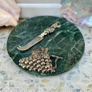 May include: A round, green marble cheese board with a silver cheese knife and a decorative silver grape cluster. The board is approximately 8 inches in diameter.