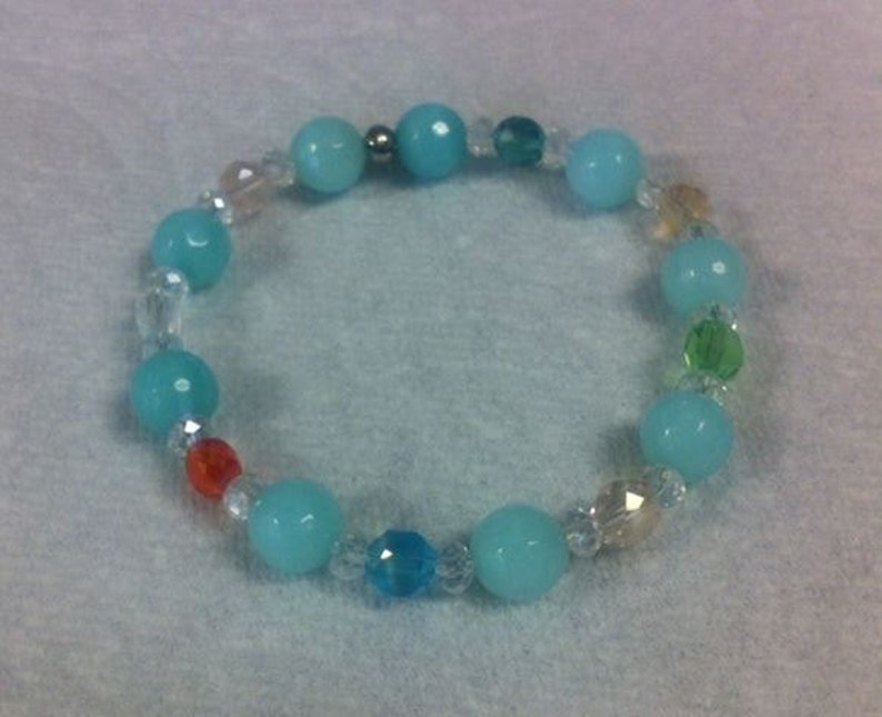 May include: A beaded bracelet featuring turquoise, clear, and colorful beads. The bracelet has large, round turquoise beads interspersed with smaller, clear, faceted beads and a few colorful accent beads. The bracelet is elastic and designed to be worn on the wrist.