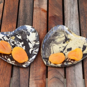 Peut inclure: Deux plats en céramique en forme de cœur avec un marbrage noir et blanc. Chaque plat contient des tranches d'abricots secs.