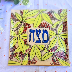 Puede incluir: Un plato cuadrado de cerámica con un diseño floral. El plato está decorado con hojas amarillas y bayas rojas. La palabra "SHALOM" está escrita en letras hebreas azules en el centro del plato.