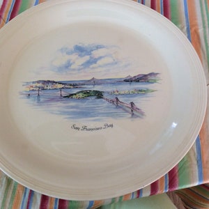 May include: A white ceramic plate with a watercolor painting of the San Francisco Bay Bridge and the city skyline. The plate has the text "San Francisco Bay" printed on it.