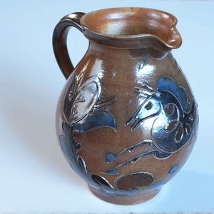 May include: A brown ceramic jug with a handle and a blue and white floral design. The jug has a rounded body and a wide mouth.
