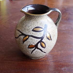 Pode incluir: Um jarro de cerâmica marrom com um esmalte salpicado e detalhes em folha de ouro. O jarro apresenta um ramo estilizado com folhas pintadas em ouro.