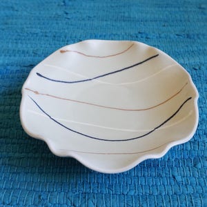 May include: A white ceramic dish with a wavy edge and an abstract design in blue and brown.