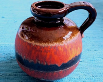 May include: A brown, orange and black ceramic vase with a rounded body and a handle. The vase has a glazed finish.
