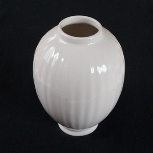 May include: A white ceramic vase with a round body and a ribbed design. The vase has a small, round base.