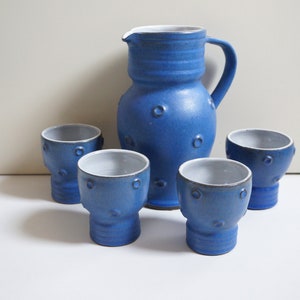 Peut inclure: Un ensemble de tasses en céramique bleue et un pichet avec des bords blancs et un glaçage bleu moucheté. Les tasses et le pichet ont un motif de cercles en relief.