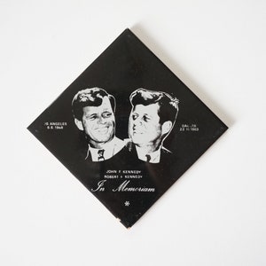 Op de afbeelding: Zwart-witfoto van John F. Kennedy en Robert F. Kennedy op een zwarte ruitvormige tegel. De tekst "In Memoriam" is onder de foto gedrukt. De data "Los Angeles 6.6.1968" en "Dal.-'63 22.11.1963" zijn in de hoeken gedrukt.