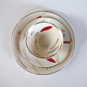 Peut inclure: Un ensemble tasse et soucoupe en porcelaine blanche avec une bordure dorée et un motif géométrique en rouge, or et vert. Le motif représente des feuilles et des lignes stylisées.