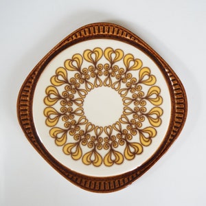 Op de afbeelding: Een bruine en witte keramische onderzetter met een geel en bruin swirl-ontwerp.
