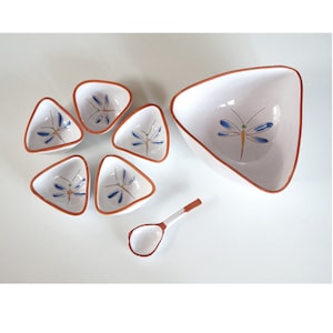 Op de afbeelding: Een set van zes witte keramische kommen met een libellenontwerp. De kommen zijn driehoekig van vorm en hebben een bruine rand. De set bevat een kleine witte keramische lepel.