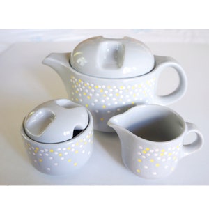 May include: A light blue teapot, creamer, and sugar bowl set with a white and yellow polka dot pattern.