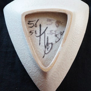 May include: White ceramic triangular dish with a textured surface. The back of the dish has a black signature that includes the numbers "56" and "55".