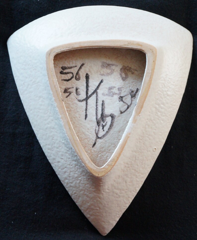 May include: White ceramic triangular dish with a textured surface. The back of the dish has a black signature that includes the numbers "56" and "55".