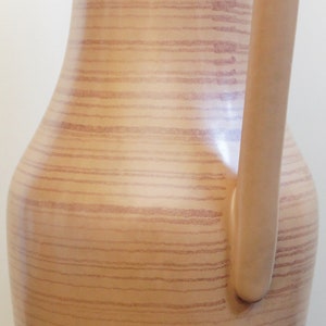 Puede incluir: Una jarra de cer&aacute;mica marr&oacute;n con un patr&oacute;n de veta de madera y un asa. La jarra tiene una base ancha y un cuello estrecho.