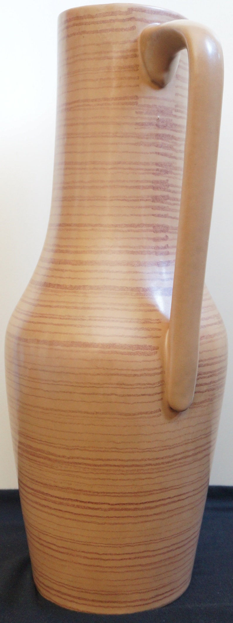 Puede incluir: Una jarra de cer&aacute;mica marr&oacute;n con un patr&oacute;n de veta de madera y un asa. La jarra tiene una base ancha y un cuello estrecho.