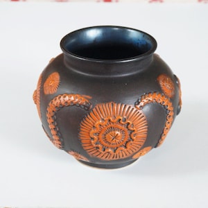 Może przedstawiać: Brązowy ceramiczny wazon z niebieską glazurą wewnątrz. Wazon jest ozdobiony pomarańczowymi wzorami kwiatowymi.