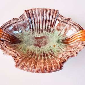 Op de afbeelding: Een bruine en groene keramische kom met twee oranje handvatten. De kom heeft een golvend, getextureerd ontwerp.