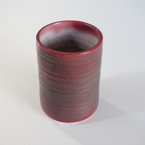 Könnte beinhalten: Eine rote Keramiktasse mit weißem Innenraum und einem strukturierten, gestreiften Design.