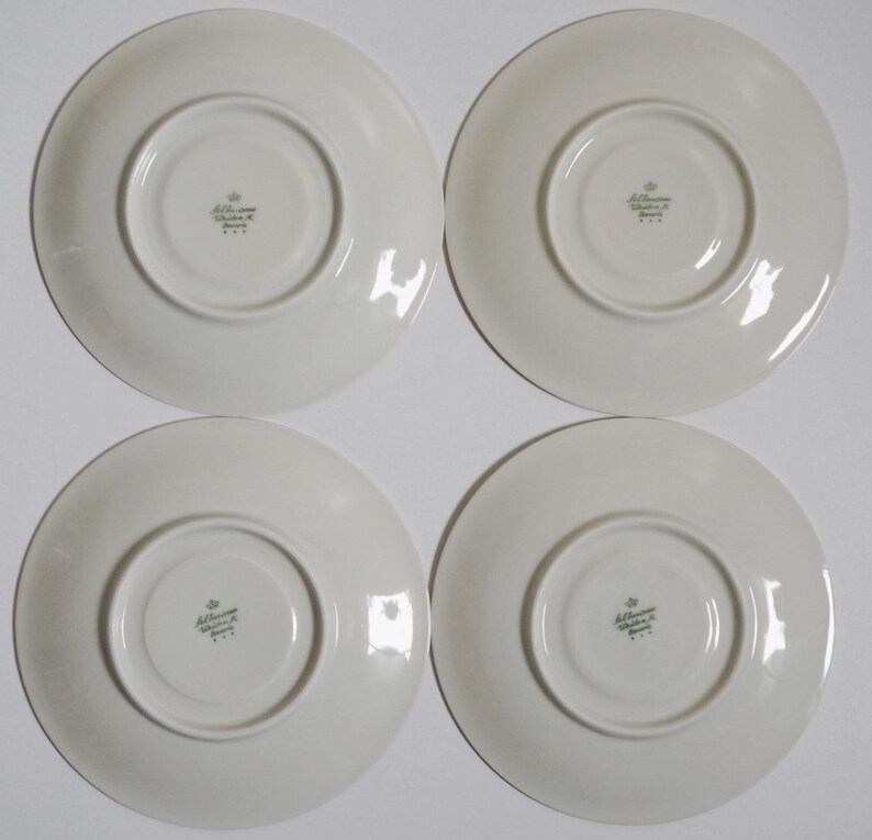 May include: Four white ceramic saucers with a green printed logo that reads "Alt Wiener Porzellan" on the bottom.