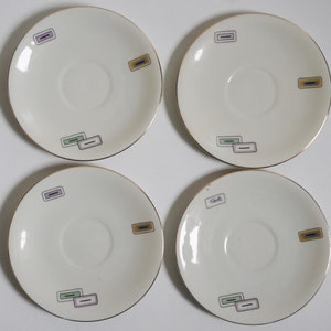 May include: Set of four white ceramic saucers with gold trim and colorful geometric designs. Each saucer has a different design.
