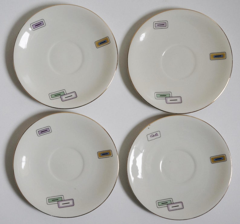 May include: Set of four white ceramic saucers with gold trim and colorful geometric designs. Each saucer has a different design.
