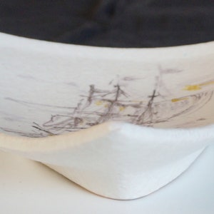 May include: White ceramic dish with a raised edge and a painted image of a ship with brown and yellow accents.