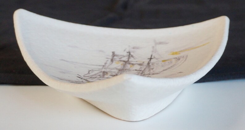May include: White ceramic dish with a raised edge and a painted image of a ship with brown and yellow accents.
