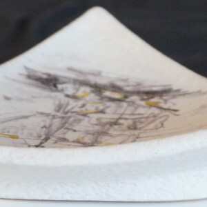 May include: A white ceramic dish with a triangular shape and a subtle, abstract design in shades of gray and yellow.